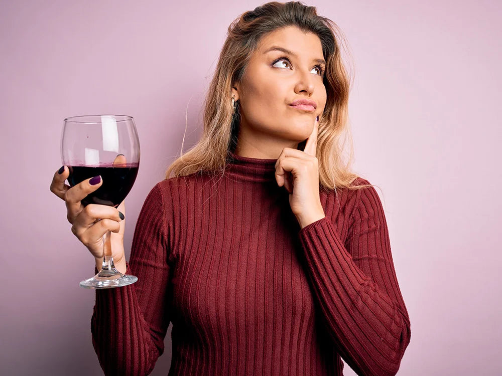 Eine junge Frau mit einem Glas Rotwein in der Hand überlegt welcher Rotwein zu ihr passt.